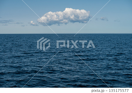 Blue ocean under a clear sky with a single cloud drifting calmly overhead 135175577