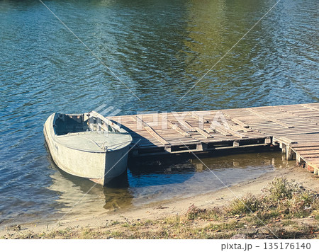 Rowboat by a wooden dock on a calm lake under clear skies. Rowboat by a wooden dock on a calm lake under clear skies. 135176140