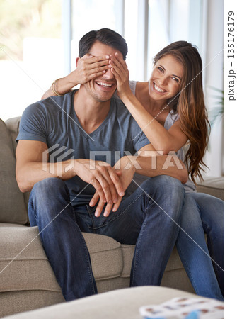 Portrait, couple and surprise with hands cover eyes for happy reveal in home living room or woman, sitting together with partner on sofa. Girl, man or playing, guess who for excited announcement Portrait, couple and surprise with hands cover eyes for happy reveal in home living room or woman, sitting together with partner on sofa. Girl, man or playing, guess who for excited announcement 135176179