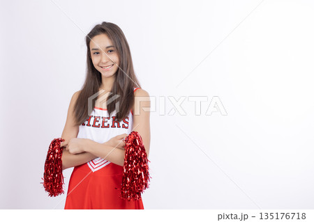 Cheerleader girl with red pom-poms standing with hands on hips 135176718