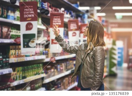 Shopping, woman at grocery store and in aisle searching and decision for product on a shelf. Customer or consumer, shopper for groceries and female person at supermarket or a shop looking for food 135176839