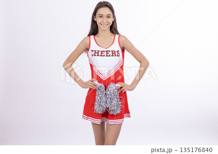 Girl in a cheerleader uniform holding red pom-poms Girl in a cheerleader uniform holding red pom-poms 135176840