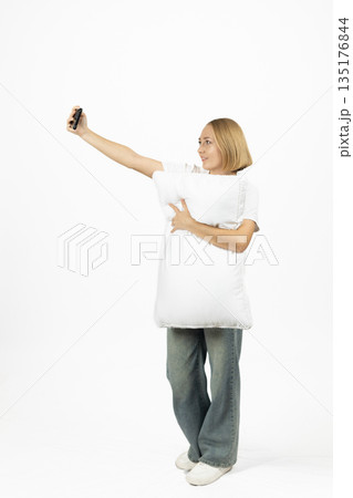 Young woman in a white sweatshirt holding a pillow Young woman in a white sweatshirt holding a pillow 135176844