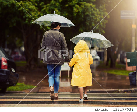 Back, raincoat or umbrella with a mother and daughter walking across a street in the city during winter. Autumn, crosswalk or park with a woman and female child holding hands while crossing a road Back, raincoat or umbrella with a mother and daughter walking across a street in the city during winter. Autumn, crosswalk or park with a woman and female child holding hands while crossing a road 135177032