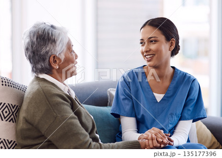 Communication, caregiver and elderly woman on lounge holding hands in living room for support. Care or healthcare, happy people and female nurse talking or consulting with a patient on a sofa. 135177396