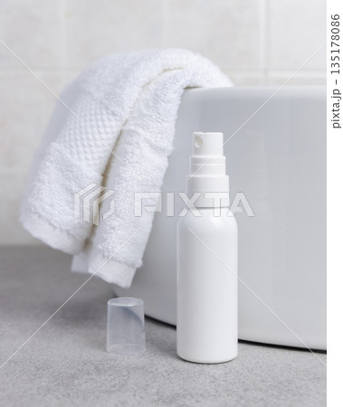 White cosmetic spray bottle on grey stone near white bath towel and basin close up, mockup White cosmetic spray bottle on grey stone near white bath towel and basin close up, mockup 135178086