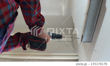A view from below of a worker holding a screwdriver while fixing paneling to a convex wall in a room, covering and securing the material to a metal profile in an indoor partition structure. 135178176
