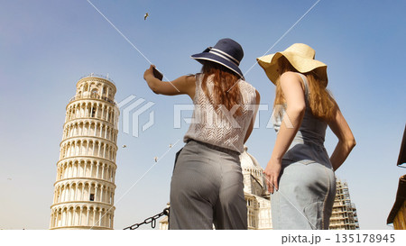 Two young women in panamas standing near the Leaning Tower and taking a photo of it Two young women in panamas standing near the Leaning Tower and taking a photo of it 135178945