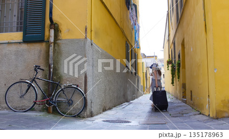 A young woman walking through the narrow yellow streets with luggage 135178963