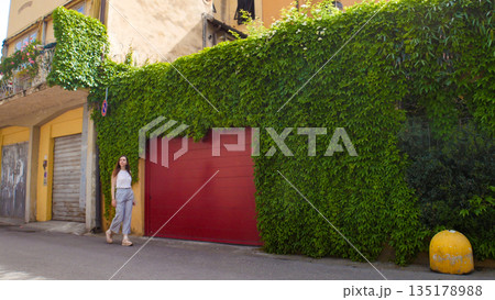 Young woman walking through the streets past the green wall Young woman walking through the streets past the green wall 135178988
