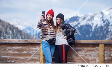 Two young women tourist standing on a background of mountains and taking a selfie on the phone Two young women tourist standing on a background of mountains and taking a selfie on the phone 135179016