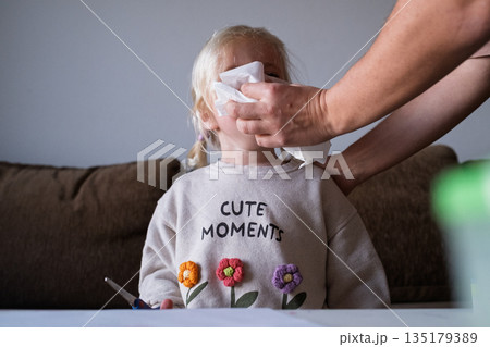 Mom caring for sick child suffering from flu or allergy, cleaning nose with handkerchief. 135179389