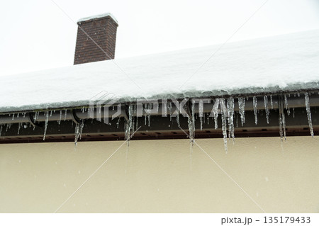Icicles on the gutter and snow on the roof of the building Icicles on the gutter and snow on the roof of the building 135179433