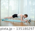 Young woman doing plank exercise at home on yoga mat. Concept of core strength, fitness, and online workout. Female holding plank position while following virtual fitness class on a tablet. 135180297