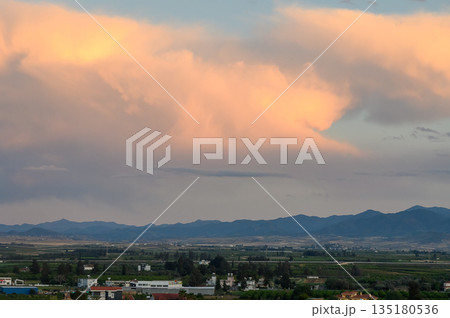 Majestic clouds gracefully billow over serene mountains at dusk, casting soft hues across the tranquil landscape and rural fields Majestic clouds gracefully billow over serene mountains at dusk, casting soft hues across the tranquil landscape and rural fields 135180536