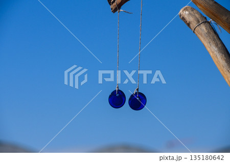 Colorful blue glass orbs dangle against a clear sky, casting playful shadows on a sunny day at a coastal location 135180642