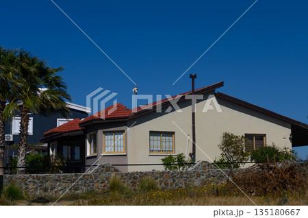 Beautiful house with red roof and palm trees under clear blue sky in a serene suburban setting 135180667