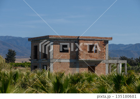 Old brick structure stands alone amidst lush greenery in a quiet landscape under a clear blue sky Old brick structure stands alone amidst lush greenery in a quiet landscape under a clear blue sky 135180681