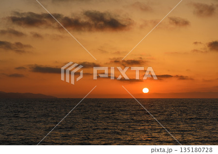 Golden hues blanket the horizon as the sun dips beneath the ocean waves during a tranquil evening 135180728