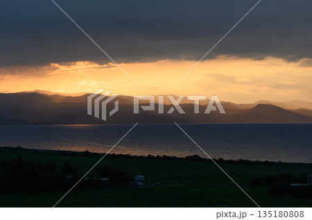 Golden hues illuminate the mountains above a calm sea at sunset in a secluded coastal region Golden hues illuminate the mountains above a calm sea at sunset in a secluded coastal region 135180808