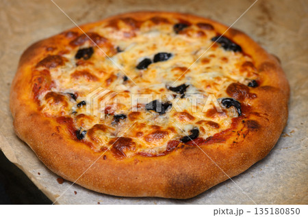 Deliciously baked pizza topped with olives and cheese, served on a rustic wooden board 135180850