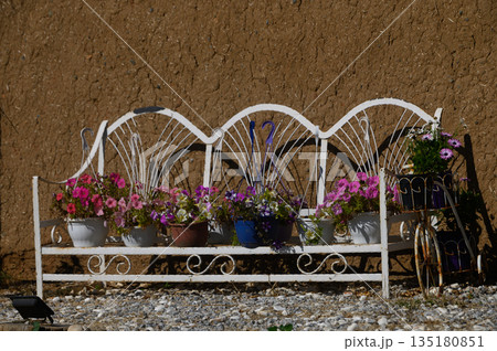 Charming outdoor bench adorned with vibrant flowers against a rustic earthen wall on a sunny day 135180851