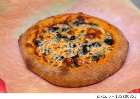 Deliciously golden-brown pizza topped with olives and cheese presented on parchment paper in a cozy kitchen setting Deliciously golden-brown pizza topped with olives and cheese presented on parchment paper in a cozy kitchen setting 135180853