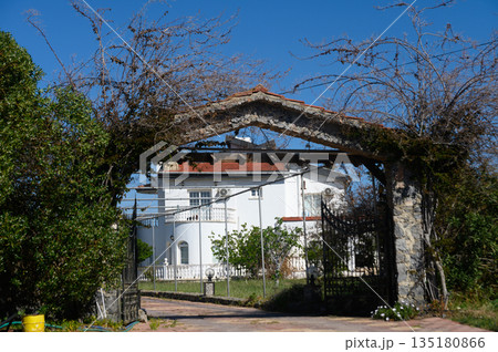 Charming white villa framed by a classic stone archway amidst lush greenery on a bright sunny day Charming white villa framed by a classic stone archway amidst lush greenery on a bright sunny day 135180866