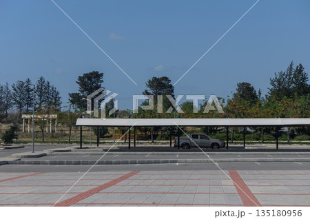 Empty parking lot with a solitary car under a canopy surrounded by trees on a sunny day 135180956