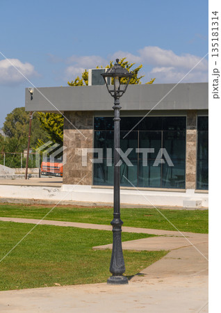 Classic street lamp stands tall beside modern architecture with vibrant green grass and clear blue sky in the background Classic street lamp stands tall beside modern architecture with vibrant green grass and clear blue sky in the background 135181314