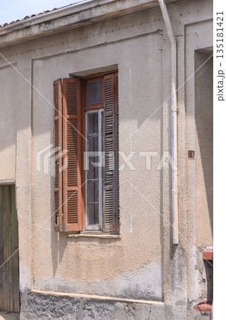 Quiet charm of a weathered building with wooden shutters in a sunlit village during midday Quiet charm of a weathered building with wooden shutters in a sunlit village during midday 135181421