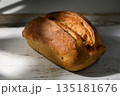 Freshly baked artisan bread rests on a rustic wooden table bathed warm sunlight 135181676