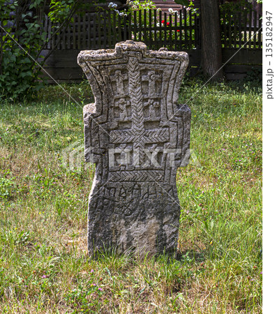 Ancient stone cross carving standing in green grass Ancient stone cross carving standing in green grass 135182947