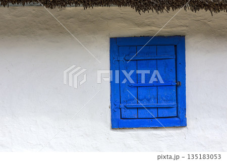 Blue window shutters on white rustic cottage wall 135183053