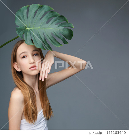 Young caucasian female with monstera leaf posing stylishly against gray 135183440