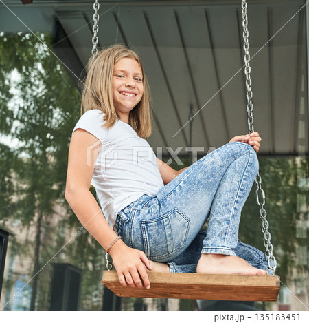 Caucasian young girl smiling on wooden swing outdoors in casual white t-shirt Caucasian young girl smiling on wooden swing outdoors in casual white t-shirt 135183451