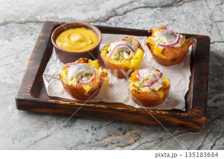 Baked potato cups stuffed with egg salad and salted herring close-up on a wooden board. Horizontal 135183684