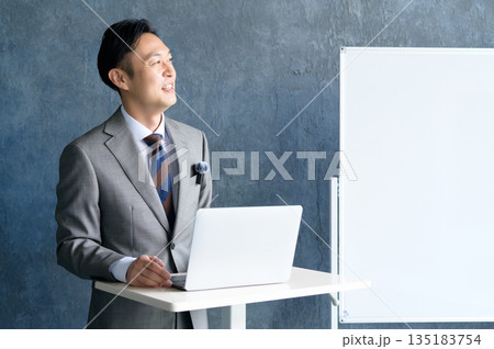 ホワイトボードの前でピンマイクをつけてプレゼンをする男性 ホワイトボードの前でピンマイクをつけてプレゼンをする男性 135183754
