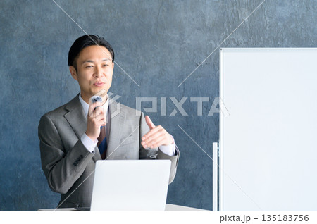 ホワイトボードの前でピンマイクをつけてプレゼンをする男性 135183756