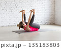 Fit Caucasian woman practice Ananda Balasana exercise indoor in loft studio. Happy Baby Pose, yoga. 135183803