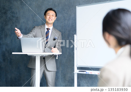 ホワイトボードの前でピンマイクを使ってプレゼンをする日本人男性 ホワイトボードの前でピンマイクを使ってプレゼンをする日本人男性 135183930