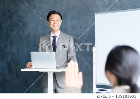 ホワイトボードの前でピンマイクを使ってプレゼンをする日本人男性 135183933