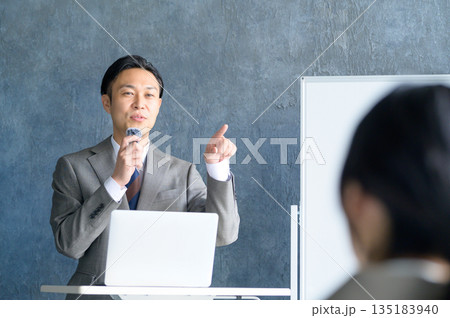 ホワイトボードの前でピンマイクを使ってプレゼンをする日本人男性 135183940