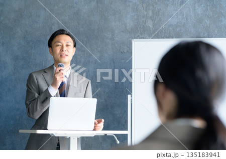 ホワイトボードの前でピンマイクを使ってプレゼンをする日本人男性 135183941
