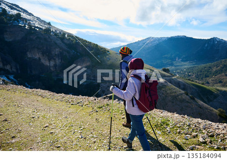 Two Hikers With Backpacks Trekking Along Mountain Trail With Scenic Valley Two Hikers With Backpacks Trekking Along Mountain Trail With Scenic Valley 135184094