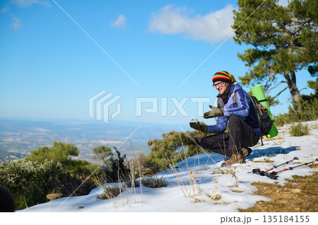 Hiker on Snowy Mountain Trail Taking in Scenic View with Backpack and Gear Hiker on Snowy Mountain Trail Taking in Scenic View with Backpack and Gear 135184155