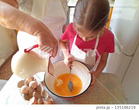 A grandmother and her granddaughter are making pancakes in the kitchen A grandmother and her granddaughter are making pancakes in the kitchen 135186219