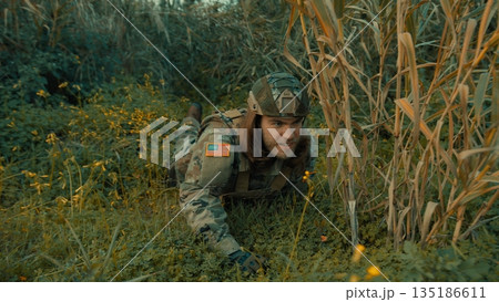 A soldier crawls on the ground in a meadow to better observe the enemy 135186611