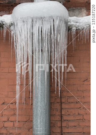 Closeup of drainpipe of building covered with thick layer of ice and icicles 135187220