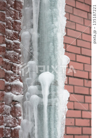 Closeup of drainpipe of building covered with thick layer of ice and icicles 135187221